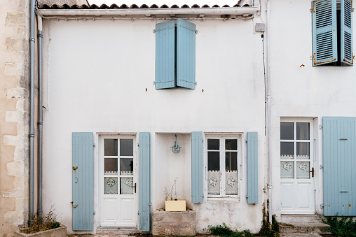 Facade of traditional house in the Island of Re with blur painted wooden shutters and lime wall.