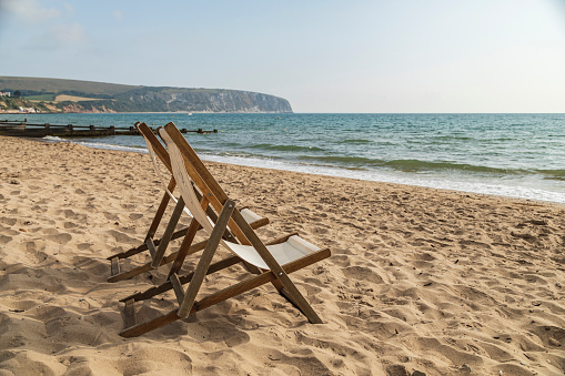 An image of a pair of deckchairs on a sandy beach in the South of England, UK. Shot with a shallow depth of field.
