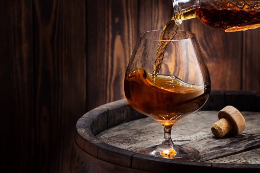 cognac pouring into snifter glass with wave surface level on old wooden barrel as table