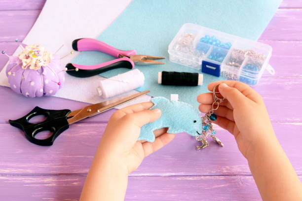 istock A child holds a dolphin in his hands. Home felt keychain with beads. Pincushion, thread, needles, pins, scissors, pliers, felt sheets, box of beads. Keychain crafts for kids diy projects 1220742837