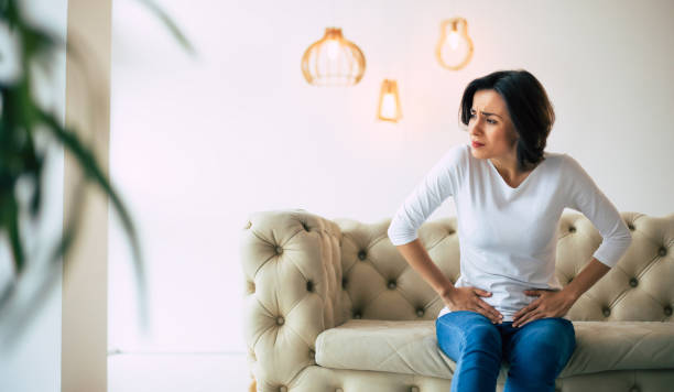 trouble menstruel. la jeune femme est assise sur un sofa et touchant son estomac inférieur tout en souffrant de douleurs d’époque. - uncomfortable photos et images de collection