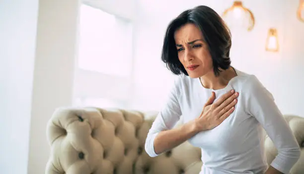 Photo of Pressure in the chest. Close-up photo of a stressed woman who is suffering from a chest pain and touching her heart area.