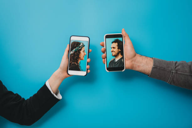 Conceptual shot of a young couple connecting together with a smartphone during social distancing Conceptual shot of a young couple connecting together with a smartphone during social distancing. They are holding smart phones against a blue background. social distancing photos stock pictures, royalty-free photos & images