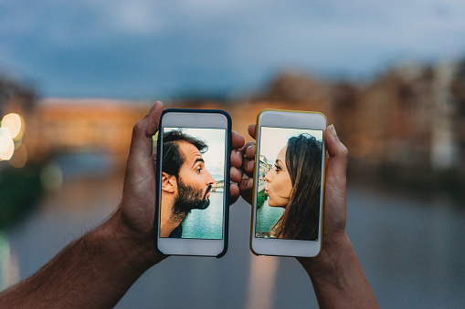 Young couple kissing via a mobile phone - Social distancing concept. During the Covid-19 Coronavirus quarantine it is important to keep a safe distance.