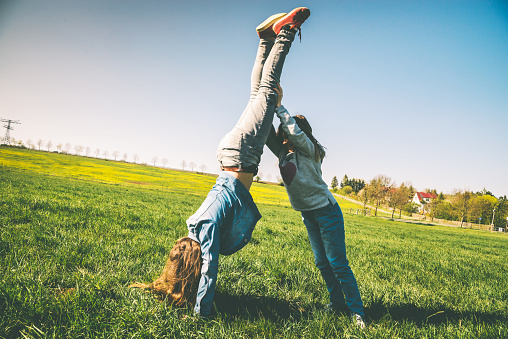 Happy girls playing on the summer meadow - trying handstand