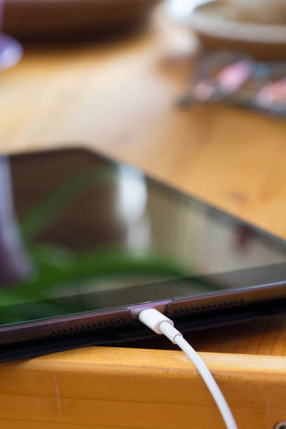 Close-up digital black tablet charging on wooden work table. Vertical.