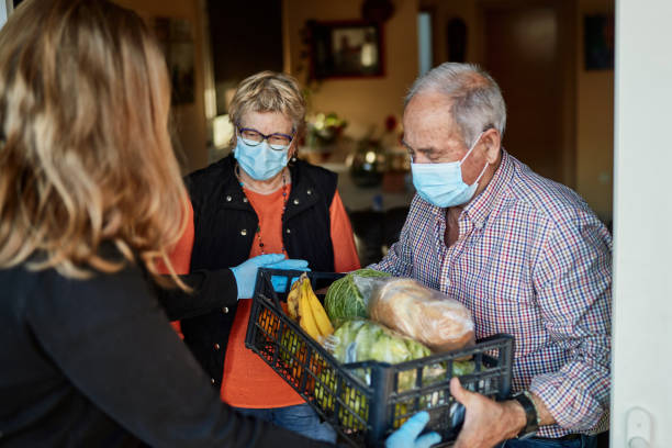 Grandchild delivers groceries to grandparents during pandemic at their home Senior couple on their 70s wearing a protective face mask picking up the groceries box that granddaughter is delivering in times of COVID-19, she is wearing mask and gloves. community outreach photos stock pictures, royalty-free photos & images