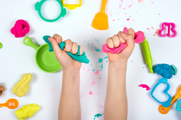 Home Education game with clay. Top view. Early development concept Little girl hands close up playing with pink and blue modeling clay on white background. Home Education game with clay. Top view. Early development concept clay stock pictures, royalty-free photos & images