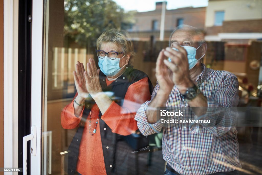 Senior couple on their 70s clapping hands at home in quarantine covid-19 Senior couple in self isolation looking through the window at home clapping. They are showing their support for all the workers and helpers who are helping during the COVID-19 outbreak. Clapping Stock Photo