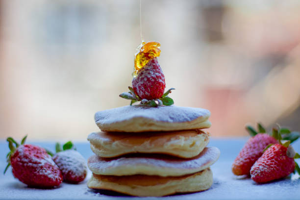 Stack of delicious fluffy pancakes with fresh strawberries and sugar and honey