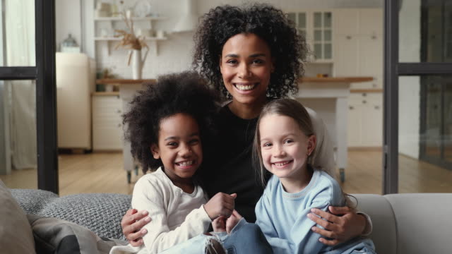 Happy mixed race family mother hugging diverse daughters at home
