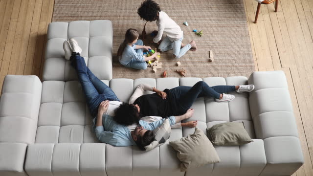 Mixed ethnicity parents with kids relaxing at home, top view