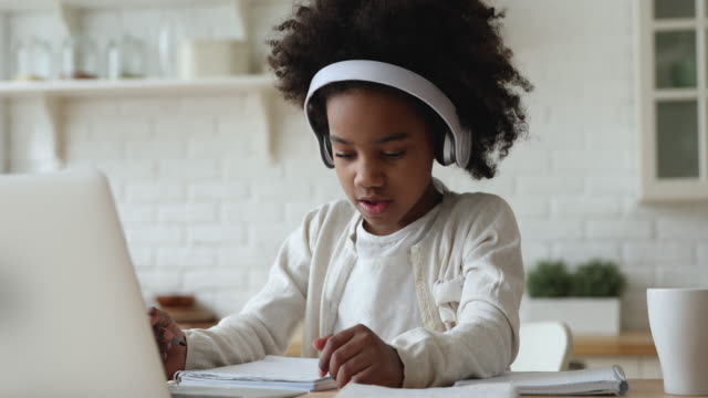 Afro american kid girl wearing headphones studying online from home