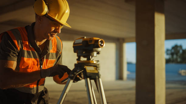 istock Inside of the Commercial / Industrial Building Construction Site: Professional Engineer Surveyor Takes Measures with Theodolite, Using Digital Tablet. In Background Skyscraper Formwork Frames Crane 1220765596