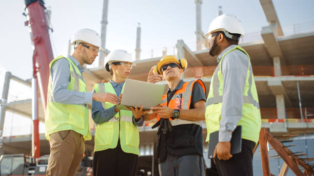 istock Diverse Team of Specialists Use Laptop Computer on Construction Site. Real Estate Building Project with Machinery: Civil Engineer, Investor, Businesswoman and Builder Discussing Blueprint Plan 1220765611
