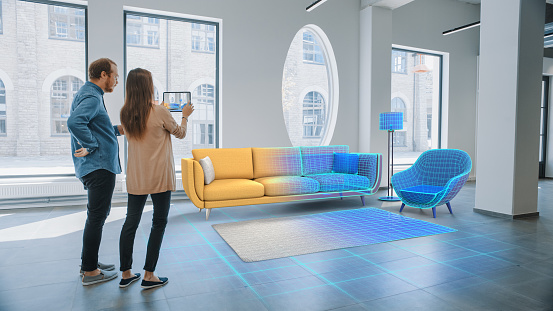Apartamento de decoración: Encantadora pareja joven utilizar tableta digital con software de diseño de interiores de realidad aumentada para elegir muebles 3D para su hogar. La gente elige sofá, mesa e iluminación para la sala de estar photo