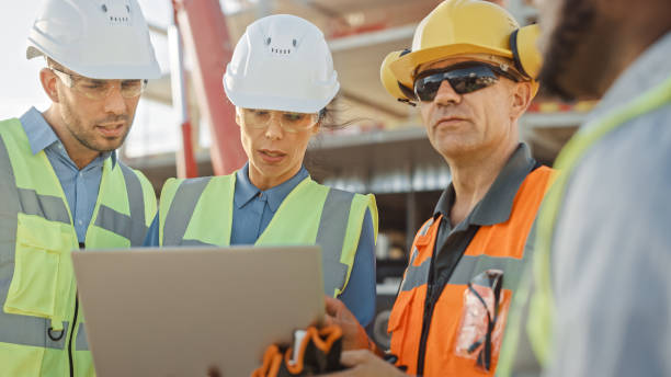 istock Diverse Team of Specialists Use Laptop Computer on Construction Site. Real Estate Building Project with Machinery: Civil Engineer, Investor, Businesswoman and Builder Discussing Blueprint Plan 1220765694
