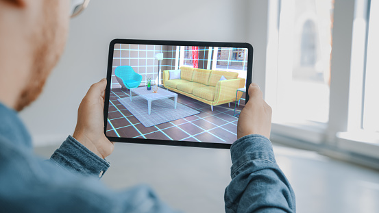 Apartamento de decoración: Man Holding Digital Tablet con AR Interior Design Software elige muebles 3D para el hogar. El hombre es elegir sofá, mesa para la sala de estar. Captura de pantalla sobre hombro con renderizado 3D photo