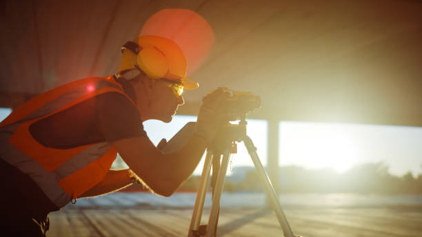 istock Inside of the Commercial / Industrial Building Construction Site: Professional Engineer Surveyor Takes Measures with Theodolite, Using Digital Tablet. In Background Skyscraper Formwork Frames Crane 1220765716