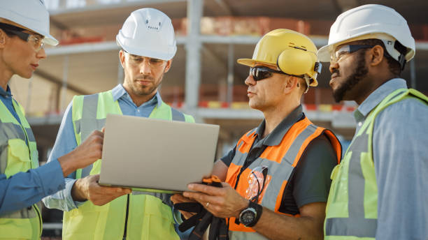 istock Diverse Team of Specialists Use Laptop Computer on Construction Site. Real Estate Building Project with Civil Engineer, Architectural Investor, Businesswoman and Worker Discussing Blueprint Plan 1220765764