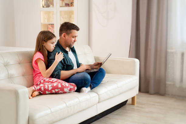 istock dad and girl work online on Notebook on couch. 1220767167