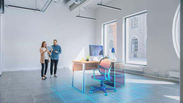 istock In Empty New Office: Female Interior Designer and Male Office Architect Talk, Use Augmented Reality Software on Digital Tablet Computer to Choose and Place 3D Furniture. VFX Special Effects 1220768115