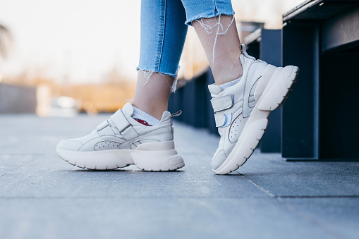 White sneakers on girl legs on the asphalt background