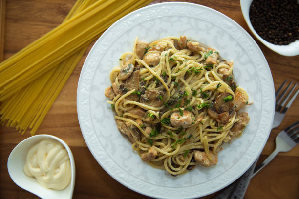 istock Mushrooms over spaghetti . Raw spaghetti pasta inside a bowl . Black pepper, Mayonnaise inside a bowl. Forks . Uncooked spaghetti . Delicious spaghetti wooden tray . 1220769936
