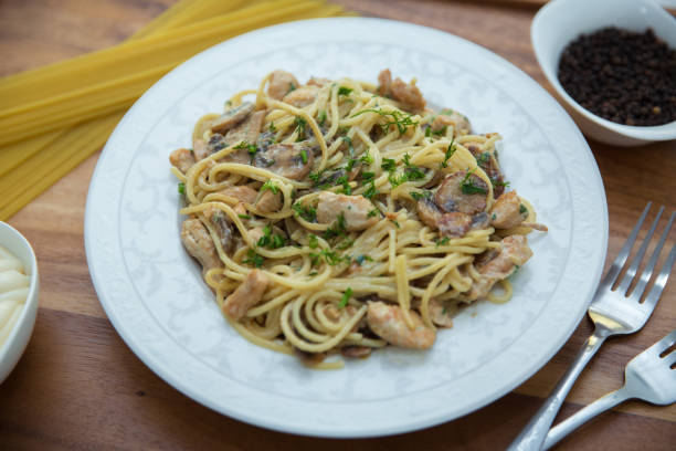 istock Mushrooms over spaghetti . Raw spaghetti pasta inside a bowl . Black pepper, Mayonnaise inside a bowl. Forks . Uncooked spaghetti . Delicious spaghetti wooden tray . 1220770156