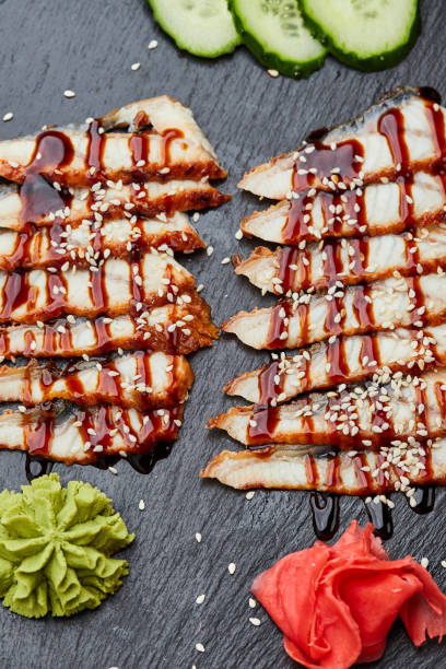 filete de anguila ahumada en rodajas con pepino fresco, jengibre encurtido y wasabi en plato de pizarra - eel trap fotografías e imágenes de stock