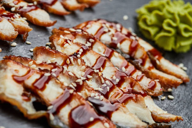 filete de anguila ahumada en rodajas con pepino fresco, jengibre encurtido y wasabi en plato de pizarra - eel trap fotografías e imágenes de stock