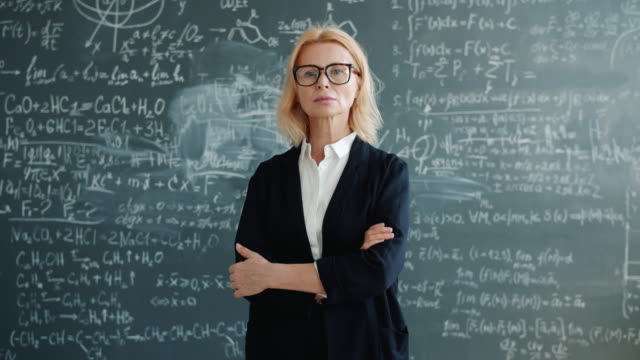 Portrait of beautiful mature woman in suit standing near chalkboard with arms crossed