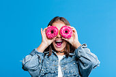 Excited teenage girl covering eyes with donuts