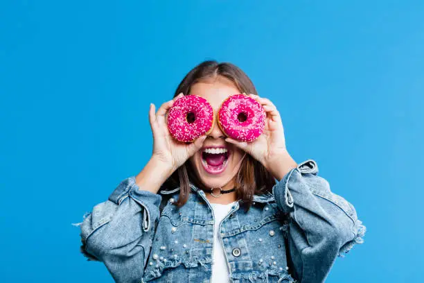 Photo of Excited teenage girl covering eyes with donuts