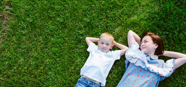 mom and son lie on their backs on a green lawn and dream happily relaxing stock photo
