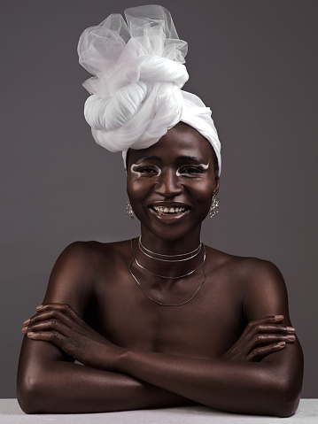 Studio portrait of an attractive young woman posing in traditional African attire against a grey background