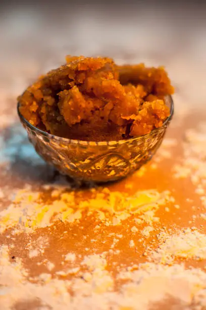 Close up of Indian Gujarati popular dish Atte ka sheera or Halwa-Karah parshad in a glass bowl on a brown surface with some spread wheat flour. Vertical shot.