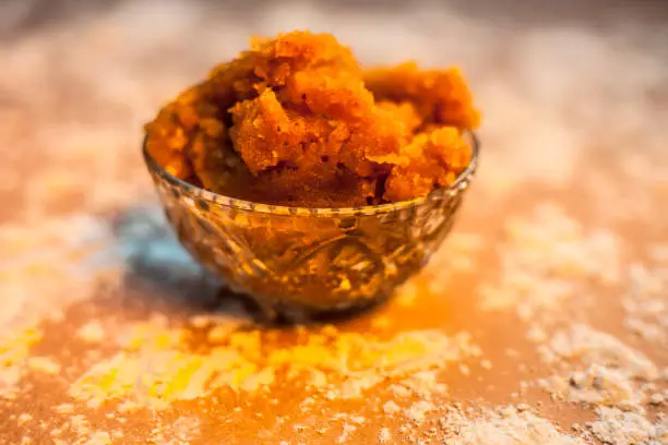 Close up of Indian Gujarati popular dish Atte ka sheera or Halwa-Karah parshad in a glass bowl on brown surface with some spread wheat flour. Horizontal shot.