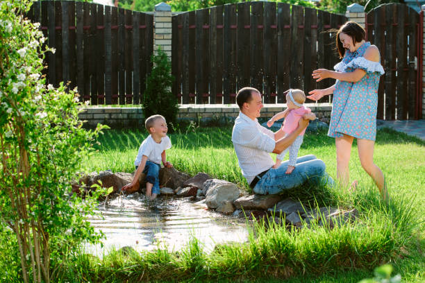 Cheerful family walking in the garden of a private house, playing on a sunlit blossoming fresh and juicy green lawn at pond stock photo