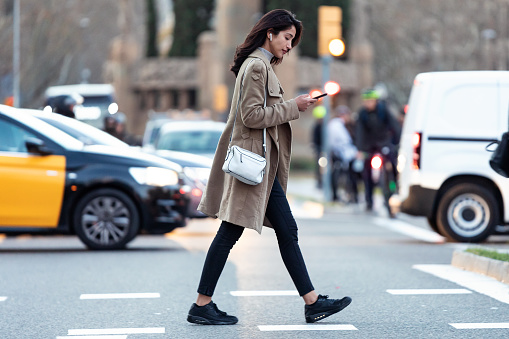 Shot of pretty young woman crossing the street while listen to music with the wireless earphones.