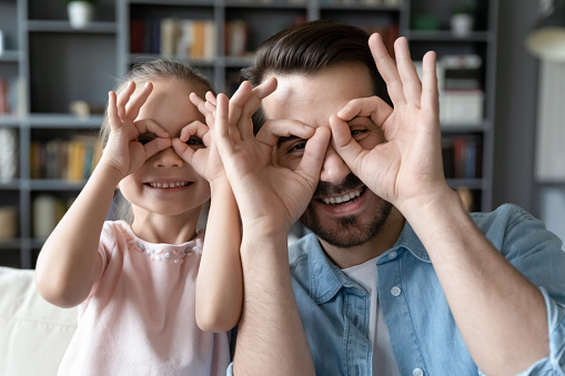 Small daughter with father making with fingers shaped like glasses