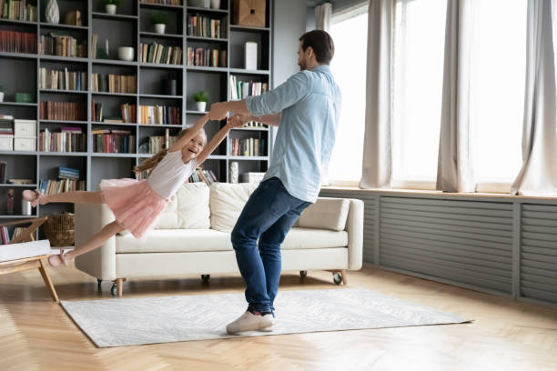 istock Father holding hands daughter spinning her having fun at home 1220791030