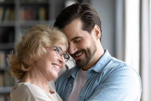 istock Millennial son and elderly mother hugging standing indoors 1220791045