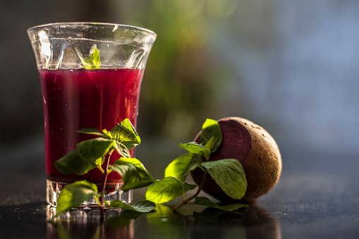 Healthy beetroot juice for weight loss in a glass on black glossy surface along with some raw fresh cut sliced beetroot vegetable some lemons, and mint leaves.Horizontal shot with blurred background.