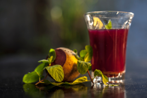 Healthy beetroot juice for weight loss in a glass on black glossy surface along with some raw fresh cut sliced beetroot vegetable some lemons, and mint leaves.Horizontal shot with blurred background.