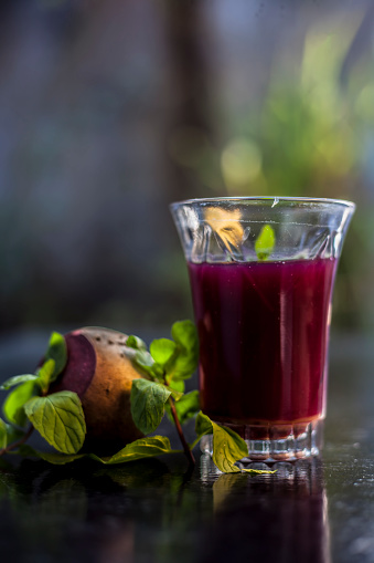 Healthy beetroot juice for weight loss in a glass on black glossy surface along with some raw fresh cut sliced beetroot vegetable some lemons and mint leaves.Vertical shot with blurred background.