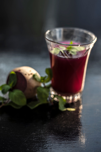 Healthy beetroot juice for weight loss in a glass on black glossy surface along with some raw fresh cut sliced beetroot vegetable some lemons and mint leaves.Vertical shot with blurred background.