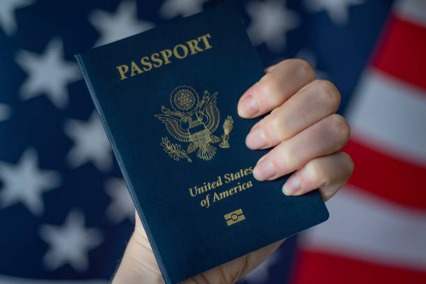 Female hand holding Passport of USA on blurred American flag background. stock photo