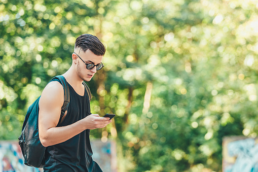 Handsome man checking mail on smartphone using application while spending time on city street, image of male in trendy outfit sending text messages via cellphone chatting in networks outdoors.