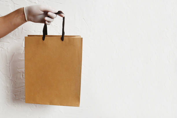 istock A man holds in his hand a brown clear empty paper bag. Delivery service concept. Packaging template mockup. 1220802375